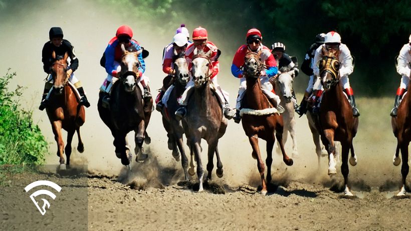 Several horses with jockeys racing on a dirt track